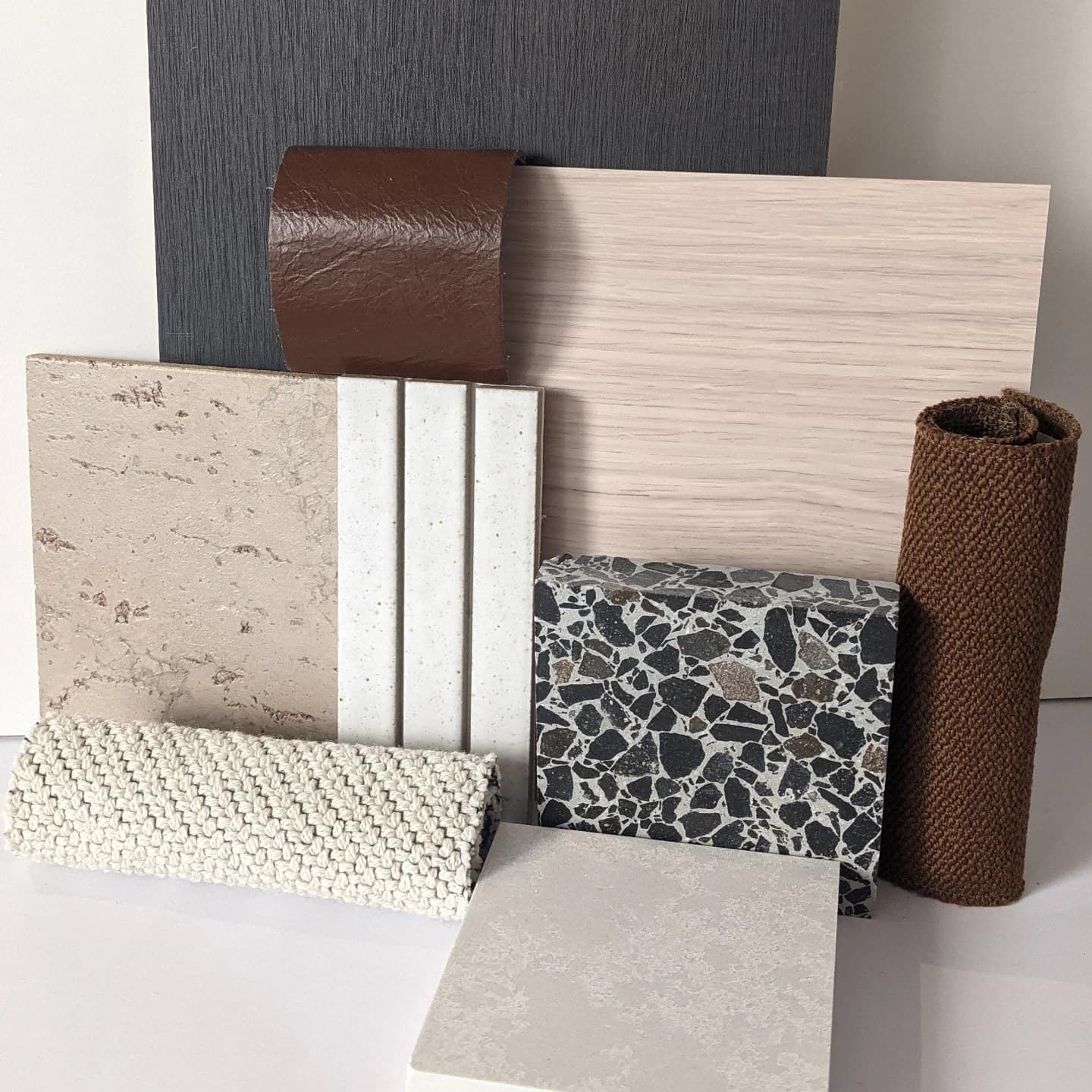 Flat lay of material samples: charcoal laminate, tan leather, oak, travertine, terrazzo and woven wool