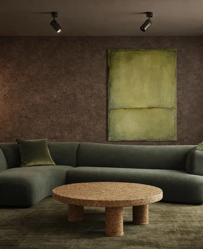 Garden studio with a cork wall, a curved green sofa, a woven rattan coffee table, an onyx side table and a lime green canvas